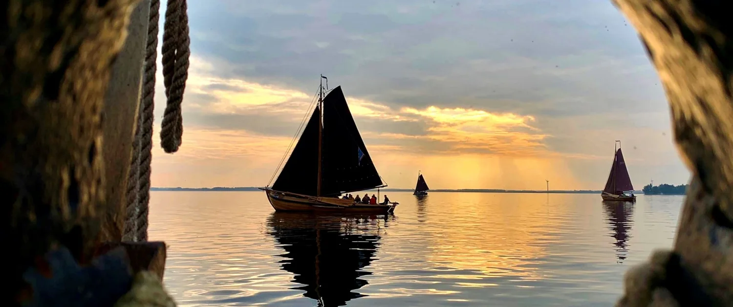 Historische botters zeilen bij zonsondergang over het Wolderwijd