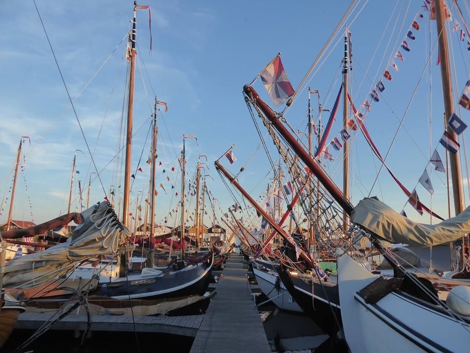 Historische rond- en platbodemjachten met vlaggen in een volle haven