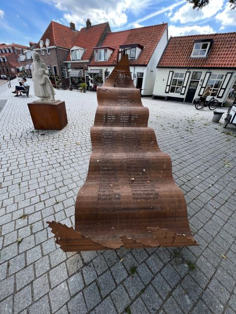 Nieuw visserijmonument met namen in een golvende metalen plaat, met het beeld van een vissersvrouw op de achtergrond